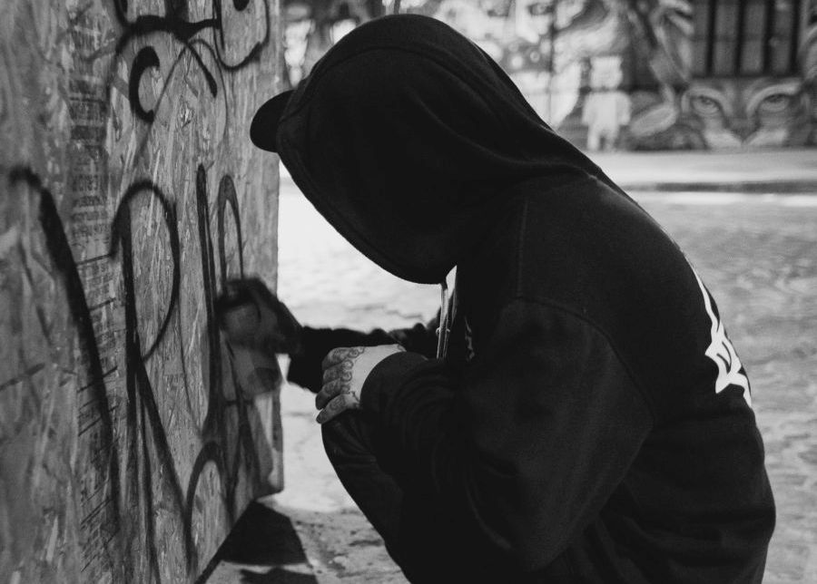 A man kneels on the ground while he is spraying a wall